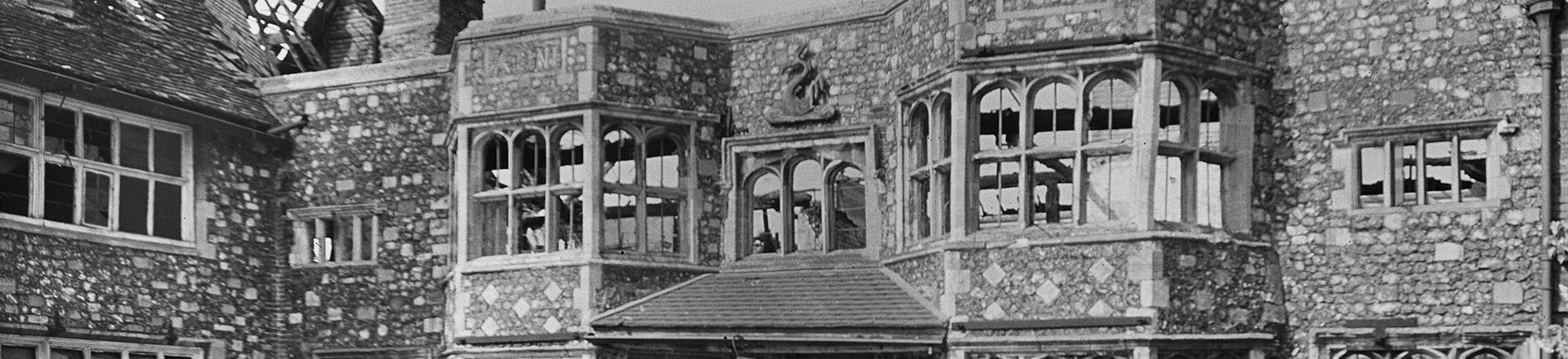 Large stone building with all window glass blown out and roof damaged.