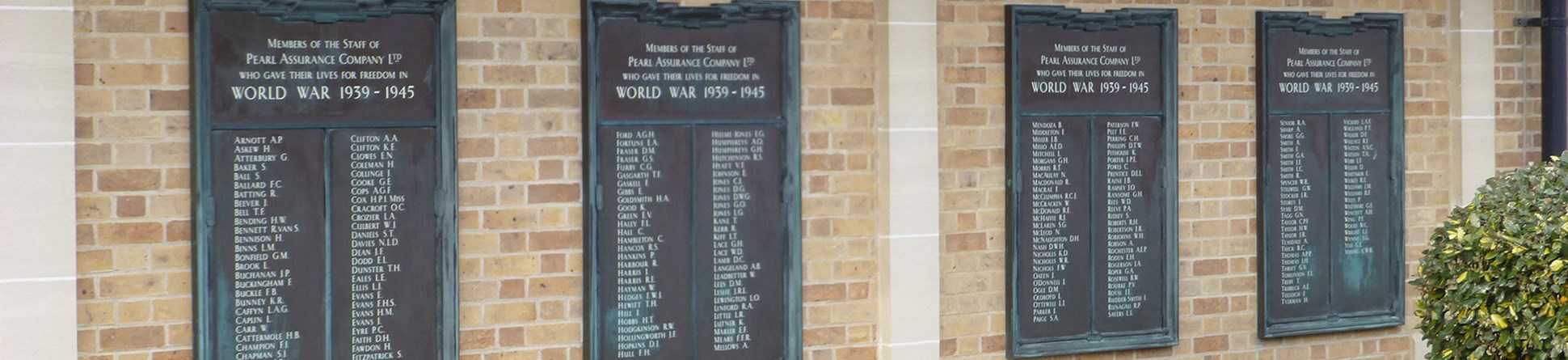 Four bronze plaques set in a brick wall with poppy wreaths placed underneath them.