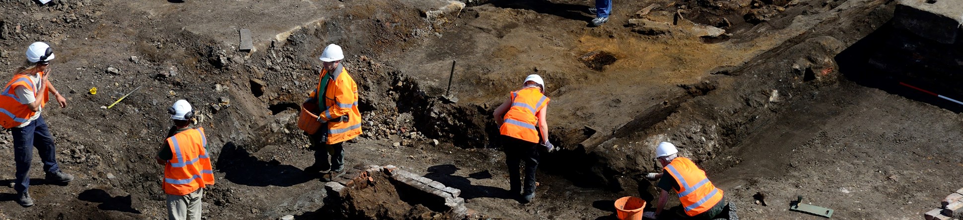 A photograph of seven people on the excavation site of a Rail Carriage and Iron Foundry site, showing building remains and footings.