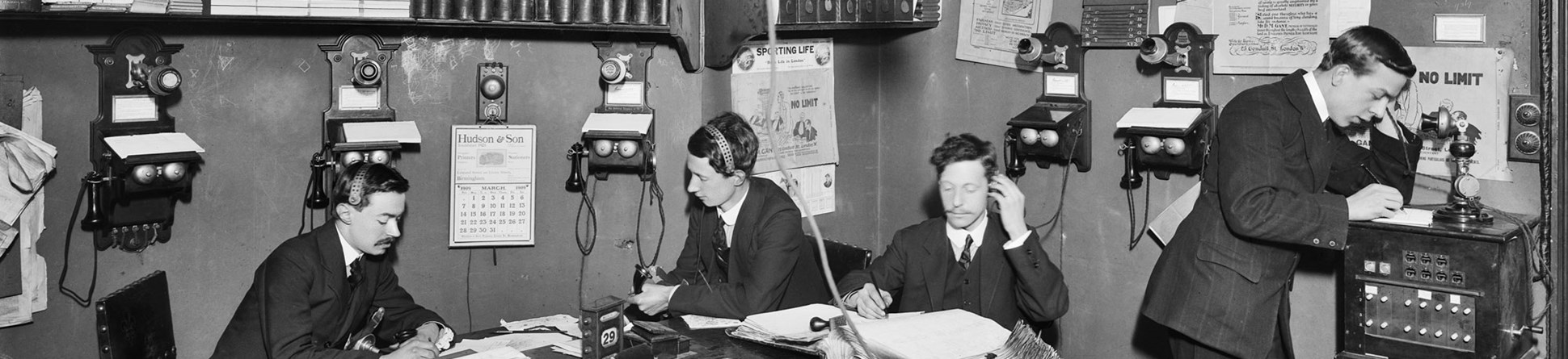 A black and white photo of the interior of a crowded office in 1909.