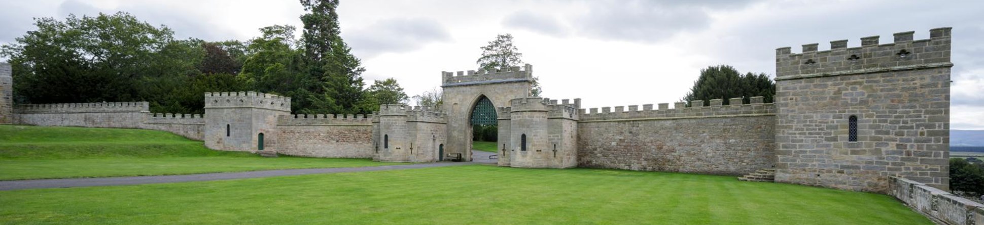 Crenellated castle wall and gateway with expansive lawns in foreground.