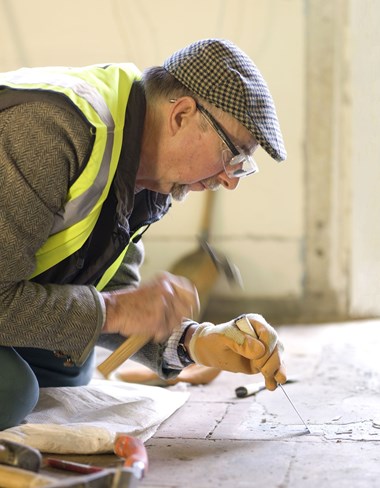 Worker removing screed from quarry tiles at Audley End House, Essex