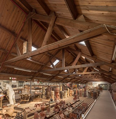 An array of terracotta chimney pots and roof tiles in a large shed.