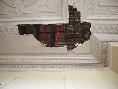 A large hole in a decorative plaster ceiling exposes pipes in the ceiling void.