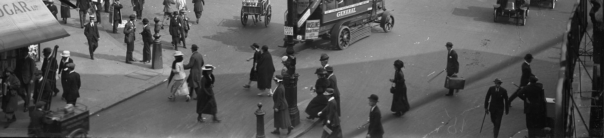 A busy street scene with pedestrians, buses and other vintage vehicles.