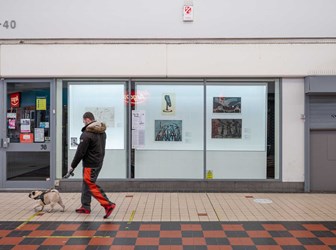 Man walking a dog past a shop where prints and drawing are displayed in the window