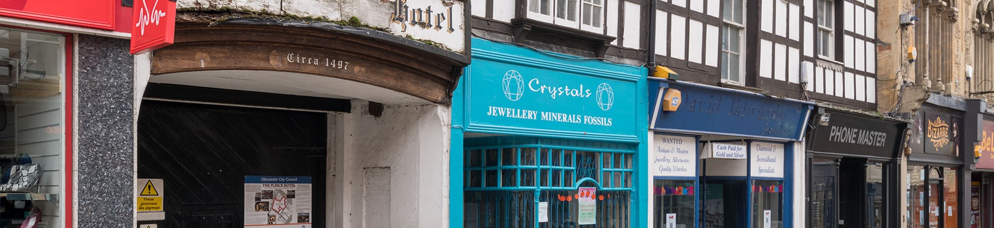 An image of the front of a historic building on a high street. The building needs repair. Its first floor is timber framed. There is an archway entrance over which is written 'circa 1497'.