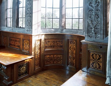 Decorative wooden wall panels in a semi-circular recess below stone carvings and leaded windows.